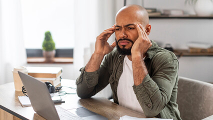 Freelance stress. Tired mature latin man looking at laptop screen and rubbing temples, sitting at...
