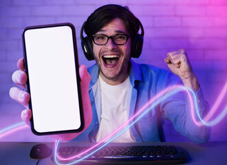Emotional gamer playing computer games, showing cell phone, mockup © Prostock-studio