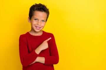 Photo portrait of adorable small schoolboy smiling point copyspace dressed stylish red knitted look isolated on yellow color background