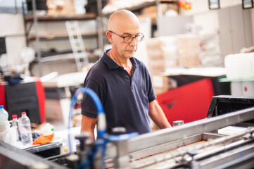 In the printing house, an experienced technician works on a screen printing machine. Production...