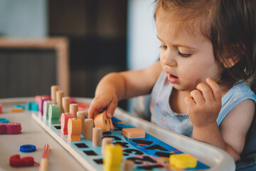 Baby girl playing with different color wooden elements making tasks for education and brain...