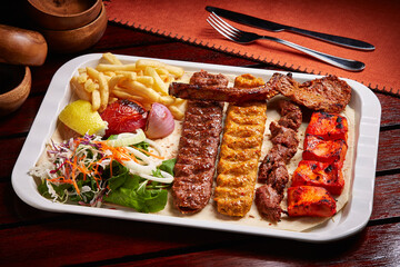 Spicy bbq Mixed Grills platter with tikka boti kababs, fries, salad served in dish isolated on table side view of middle east food