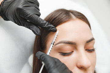 A cosmetologist makes anti-aging injections against wrinkles on the forehead on the face of a...