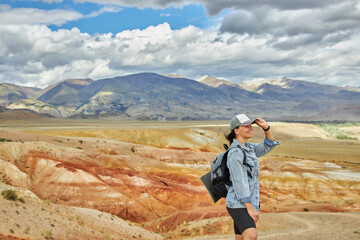 woman tourist in jeans jacket stands against backdrop of sandy hilly landscape. Sights of Russia, Siberia and Altai Republic, mars field. Tourism, travel and adventure. Kosh-agach, Chagan-Uzun
