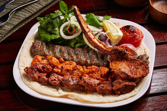 Spicy Mixed Grills platter with tikka boti kabab, salad, lemon and bread served in dish isolated on table side view of middle east food