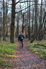 Obraz premium A man walks a dog in an autumn forest park, plays with a stick, drinks coffee in a reusable thermocup