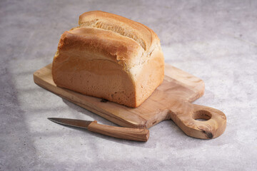 One whole freshly baked loaf of white wheat bread on baking paper on wooden board