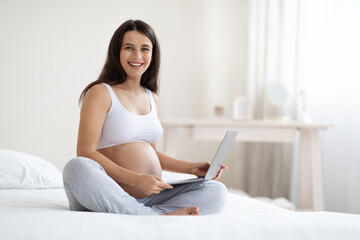 Happy pregnant woman using laptop at home, copy space