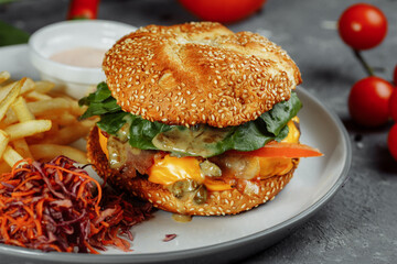 Turkey burger on a bun with cheese, lettuce, tomatoes and fresh cucumber. Burger with cutlet of turkey meat on a gray background with french fries