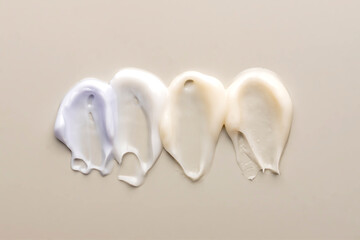 Group of cream strokes of various colours on beige background. Smear of lotion, hand or face cream in similar shapes and sizes. Skincare cosmetics product. Cosmetology, wellness, beauty concept.