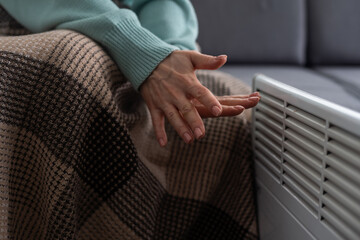 Woman warming hands near electric heater at home, closeup