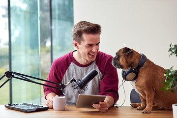 Man With Pet French Bulldog Wearing Headphones Recording Podcast Or Broadcasting On Radio At Home
