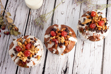 sweet bread for the Christmas holidays round and oval with dry fruits walnuts almonds cream icing cherries raisins on milk white countertop and decorated with dried flowers    