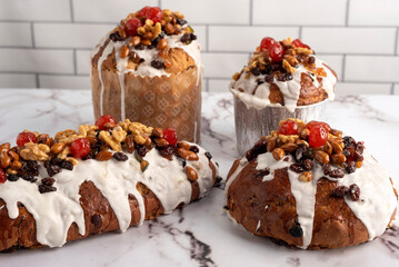 sweet bread for the Christmas holidays round and oval with dry fruits walnuts almonds cream icing cherries raisins on milk white countertop and decorated with dried flowers    