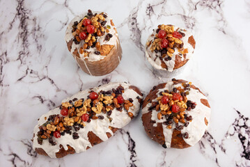 sweet bread for the Christmas holidays round and oval with dry fruits walnuts almonds cream icing cherries raisins on milk white countertop and decorated with dried flowers    