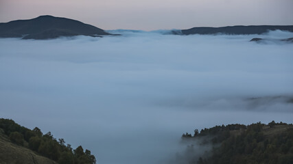 Low clouds in the mountains filled the entire valley and mountain peaks and hills stick out above the clouds, on an autumn twilight evening