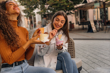 Two girls are having fun and eating delicious ice-cream in the cafe garden on a sunny day.