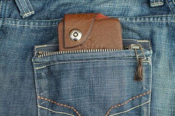 part of a brown leather closed men's wallet for money in a fashionable and stylish blue denim pants...