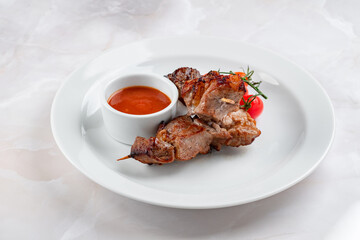 Grilled lamb kebab served on a white plate. Pieces of meat on skewers with ketchup
