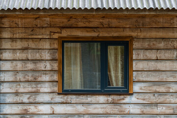 One window on the wooden facade of a rustic house made of wooden beams in a mountains Carpathian village, Western Ukraine, Europe