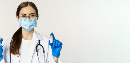 Covid-19 vaccination and healthcare concept. Young doctor in medical mask showing syringe and...