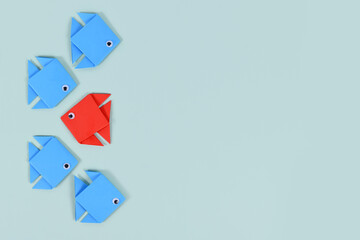 Red paper fish swimming swimming against the current in opposite direction of blue fish