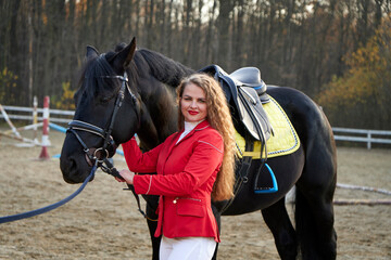 Beautiful  young horse woman in a red suit near a stallion. Young sexy woman standing near a horse...