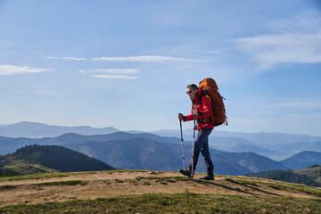 Young sporty hiker hiking in the mountains with his backpack on a bright sunny day. Picturesque...
