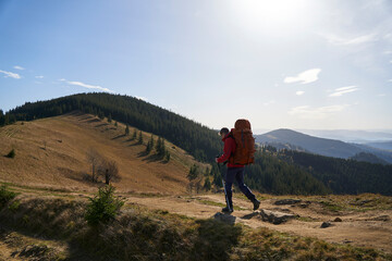 Fototapeta premium Young sporty hiker hiking in the mountains with his backpack on a bright sunny day. Picturesque mountain landscape.Concept of traveling in the mountains. Hiking in the mountains with a backpack 