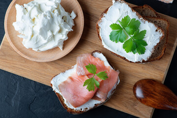 Home made bread on a wooden cutting board with curd cheese and pink salmon