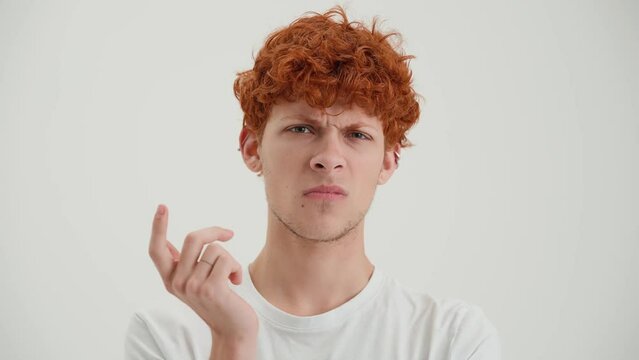 Frustrated red haired young man saying what at the camera in the white studio