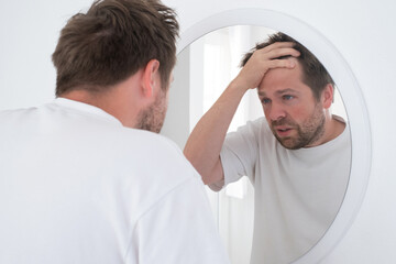 Tired mature caucasian man is looking at the mirror.