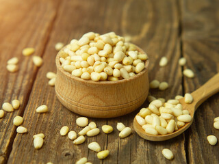 Heap of raw pine nuts in a wooden bowl and spoon. Peeled pine nuts on an old wooden table.
