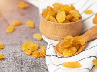 Golden raisins in a wooden bowl and a spoon on a dark concrete background. Dried grapes or raisins.