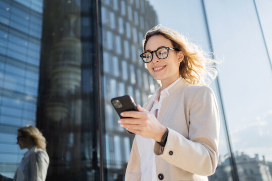 Uses a phone device in his hands, communicating with a colleague. A woman with glasses is a marketing expert working in an office.