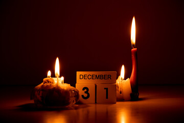 December 31 is written on wooden cubes that stand in the dark on the table next to candles at home,...