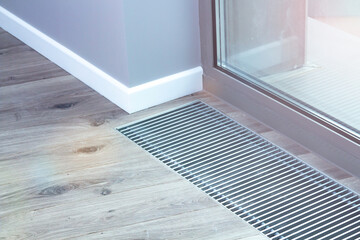 Floor convector heating metal grate built into the floor next to the window.