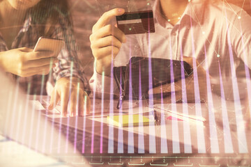 Double exposure of man and woman on-line shopping holding a credit card and forex graph hologram drawing. Stock market E-commerce pay on-line concept.