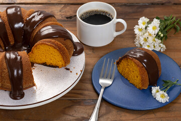 carrot cake with chocolate icing, slice of cake on a blue plate on a rustic wooden table, coffee mug