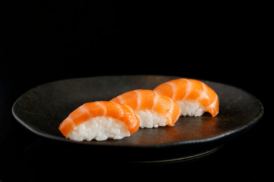 Gray plate with 3 pieces of raw salmon rice sushi on a black background