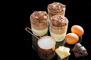 Three white and black chocolate mousse in glasses on a black background, with ingredients