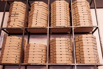 food delivery service. tall stacks of flat brown cardboard pizza boxes on metal shelf ready for delivery. craft packing boxes with pizza in stock in storage