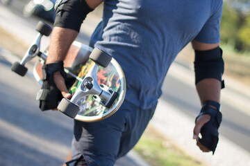 Close-up of skateboard in male hands. Man walking and holding colorful longboard on sunny summer...