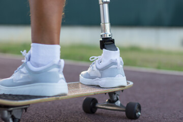 Close-up of prosthetic male leg on skateboard. White shoes and longboard, man training in park. Sport, disability concept - obrazy, fototapety, plakaty