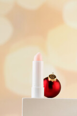 Pink moisturizing hygienic lipstick on a pedestal with a Christmas ball. Lip care in winter.