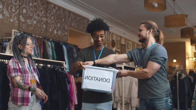 Diverse volunteer receive boxes with donated clothes in second-hand store. Realtime