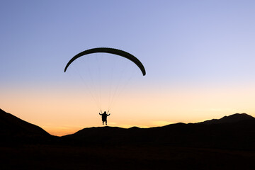 Fototapeta na wymiar Silhouette of a Paraglider and Mountains Against Cloudless Sunset