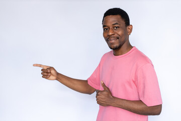 Portrait of pleased African American man pointing finger at ad. Happy young male model with short dark hair in pink T-shirt looking at camera, smiling with thumb up. Advertisement, approval concept