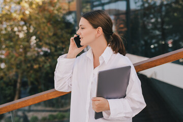 Young business woman with laptop using her smartphone.