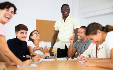 Group of interested women and men of different ages and nationalities sitting around table and...